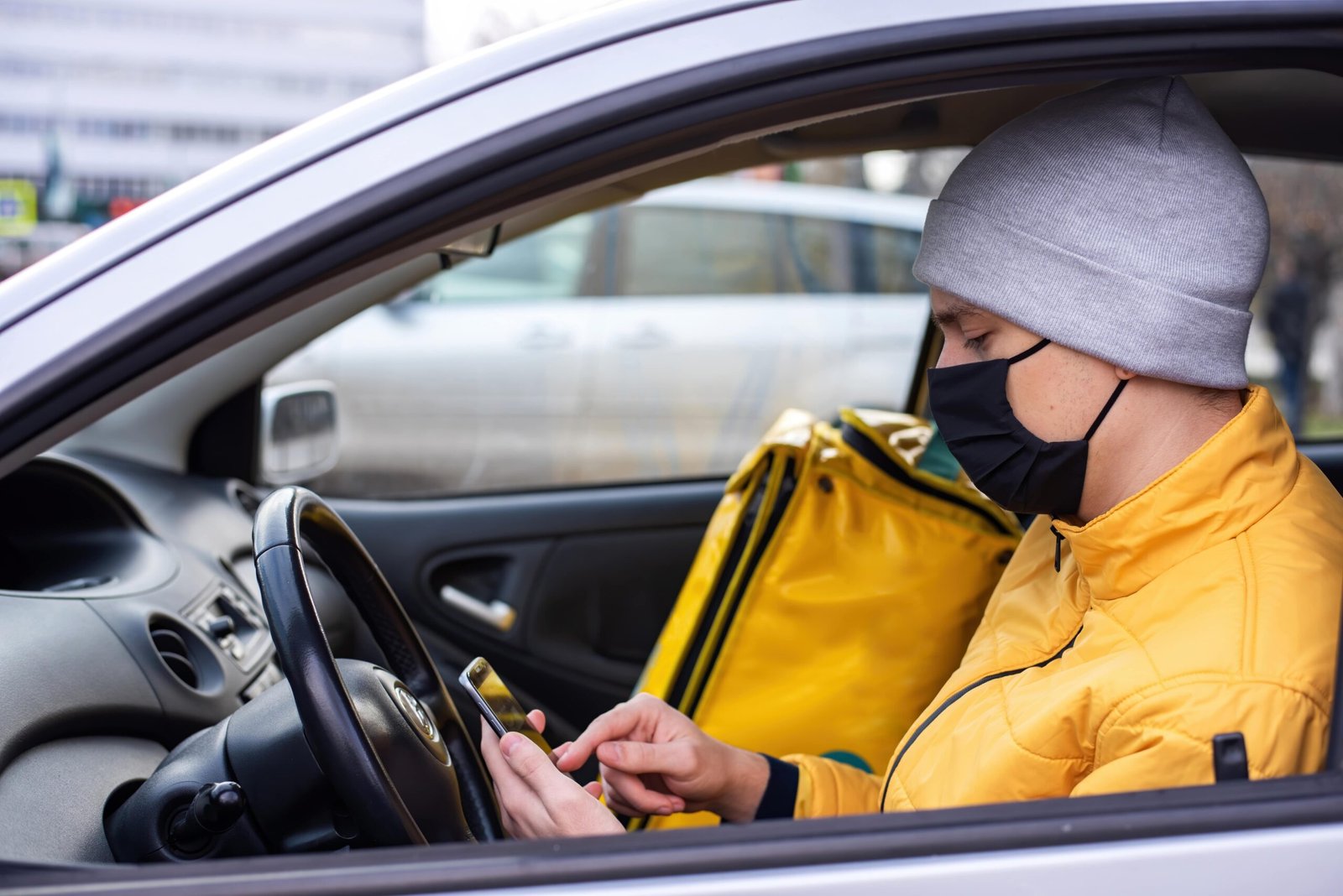 courier-car-with-black-medical-mask-is-his-phone-delivery-backpack-seat-food-delivery-service-min